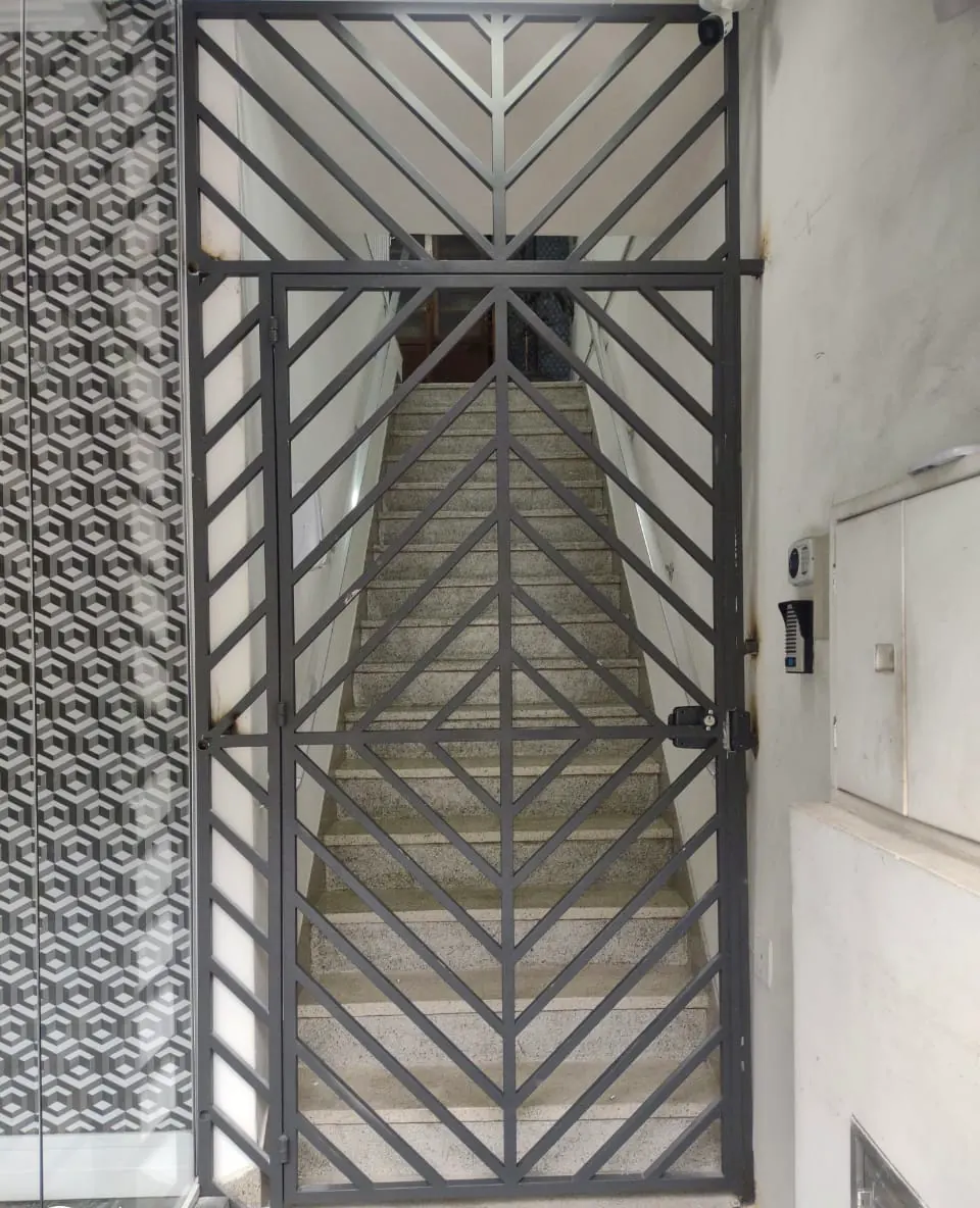 Portão de grade com desenho em diagonais na entrada de uma escada